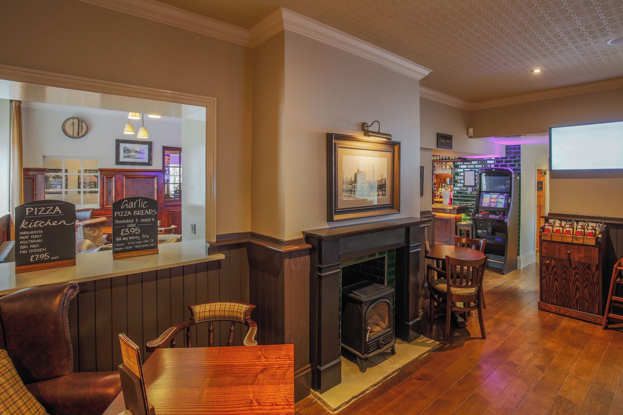 A cozy pub with a bar area, a fireplace, and a gaming machine.