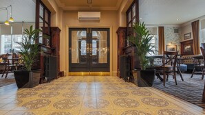 A hotel lobby with a patterned tile floor, a central double door, and potted plants on either side. - Norfolk Arms Hotel (Glossop)