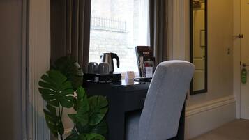 A hotel room with a desk, a chair, a coffee maker, a menu, and a large mirror.