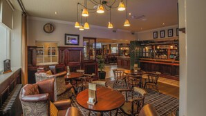 A bar area with wooden furniture, a bar counter, and hanging lamps. - Norfolk Arms Hotel (Glossop)