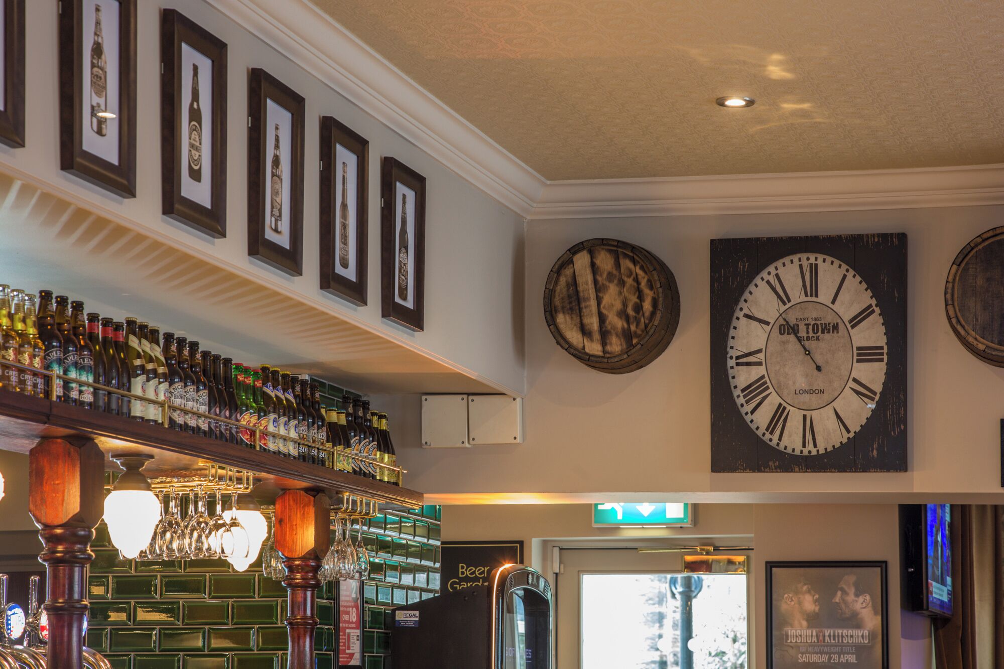 Un espace bar agrémenté d’une horloge, de bouteilles de bière encadrées et d’un panneau indiquant la présence d’un jardin à bière.