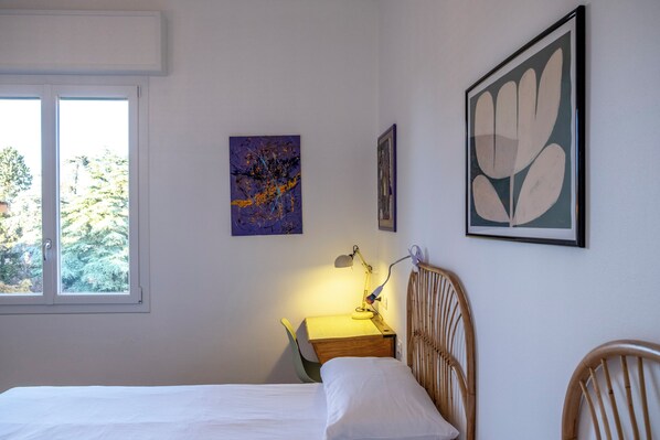Un dormitorio con cama, un escritorio con lámpara y dos cuadros en la pared.