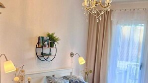 Een keurig opgemaakt slaapkamer met een gestreept dekbedovertrek, bedlampen, een kroonluchter en uitzicht op de omgeving door een groot raam.