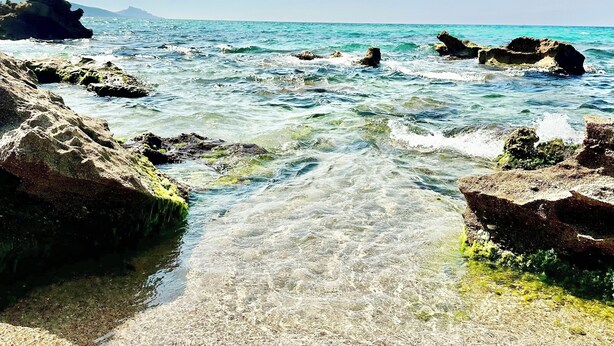 A clear view of a rocky shoreline with calm waters and a distant mountain.