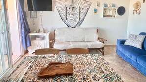 A living room with a patterned rug, a wooden coffee table, a blue sofa, a white armchair, and a TV mounted on the wall.