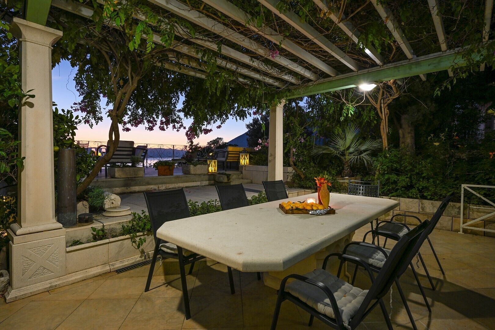 An outdoor patio with a table and chairs, surrounded by greenery and a pergola.