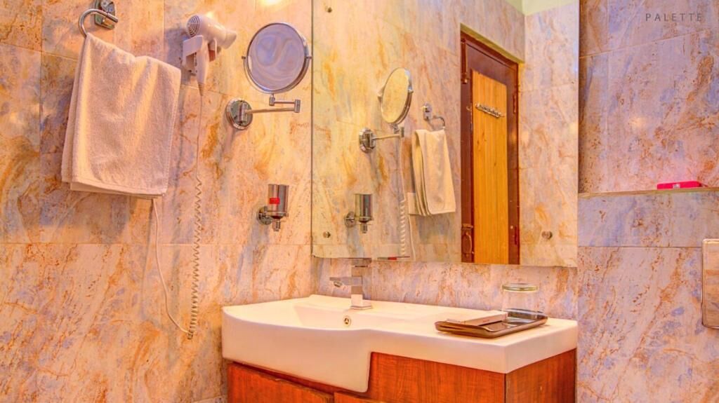 A bathroom with a marble sink, two towel racks, a mirror, and a door.