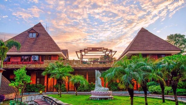 A hotel with two main buildings, a central structure, and a well-maintained garden with palm trees and a statue.