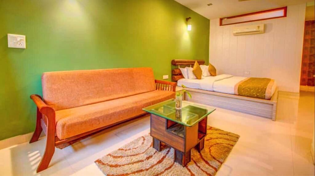 A room with a sofa, a small glass-top table, and a bed with pillows.