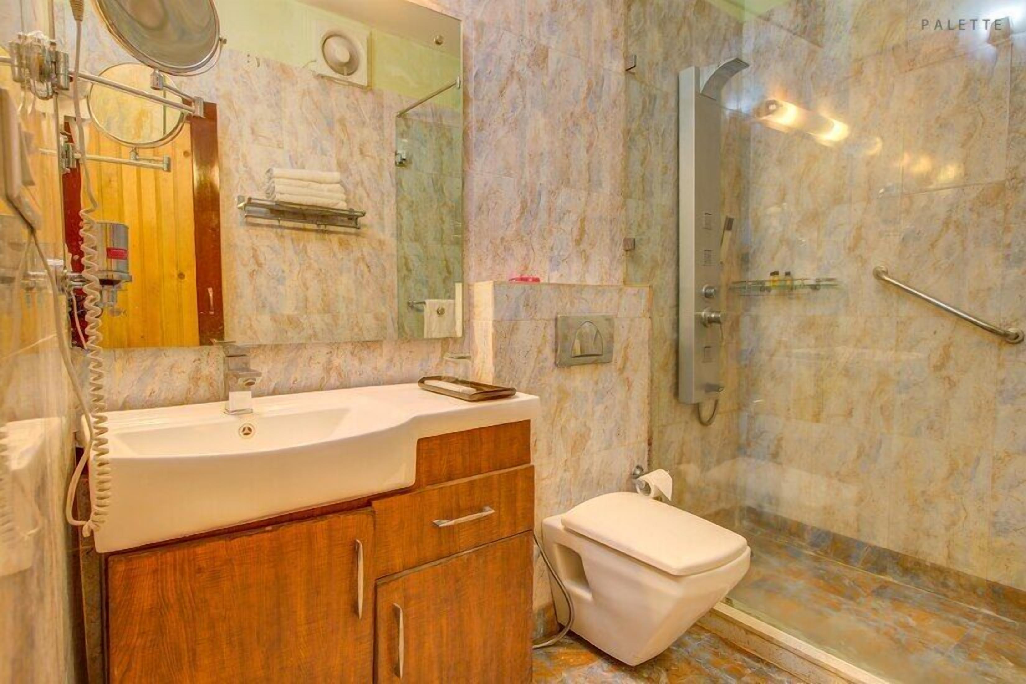 A bathroom with a marble wall, a sink, a mirror, a towel rack, and a shower area.