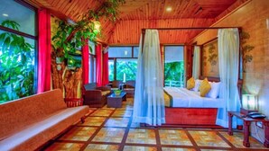 A bedroom with a canopy bed, a sofa, and a view of greenery outside.