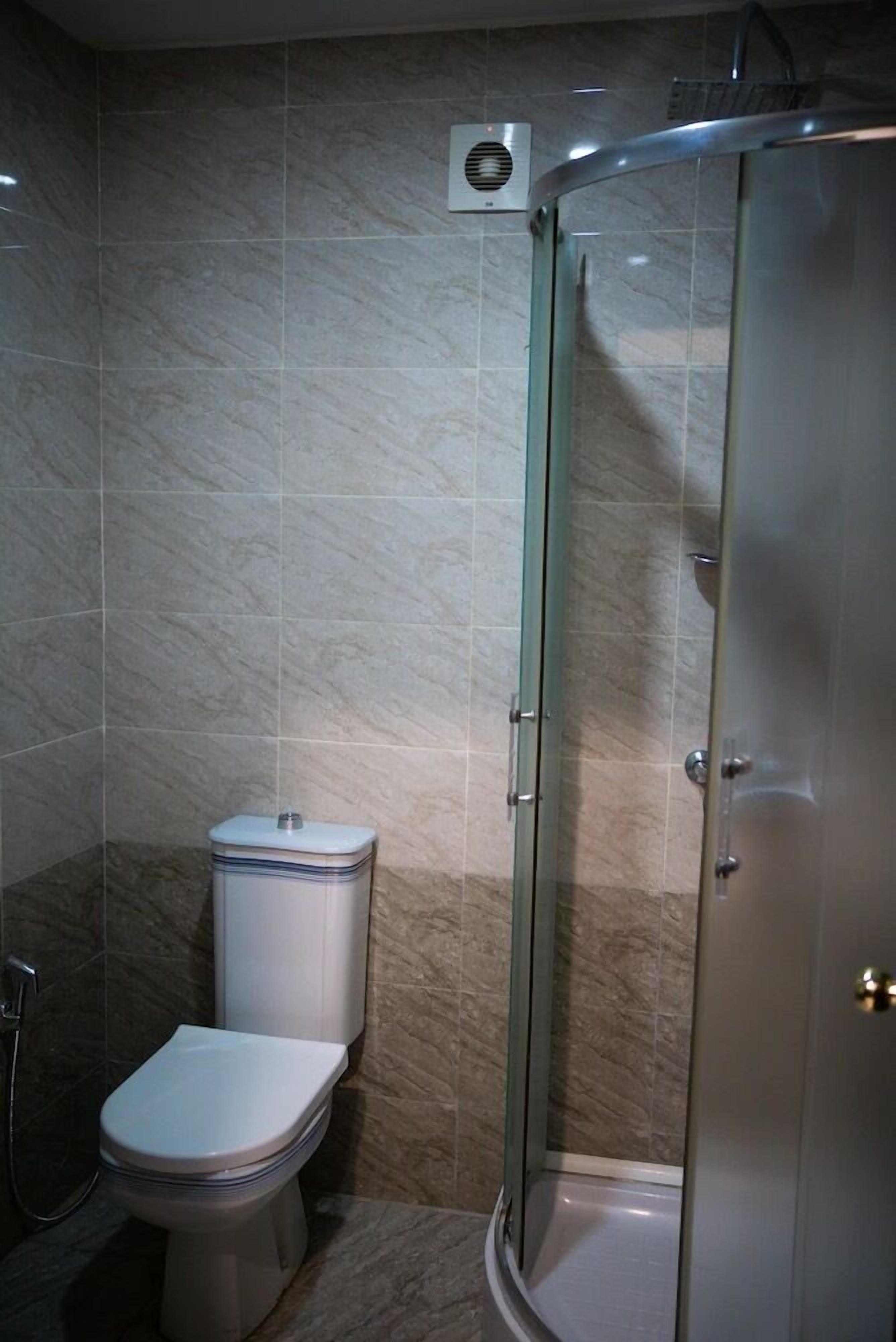Een badkamer met toilet, douchecabine en een ventilatie-unit aan de muur.