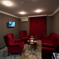 Una habitación con tres sillones rojos, una mesita con un centro de mesa floral y un televisor montado en la pared.