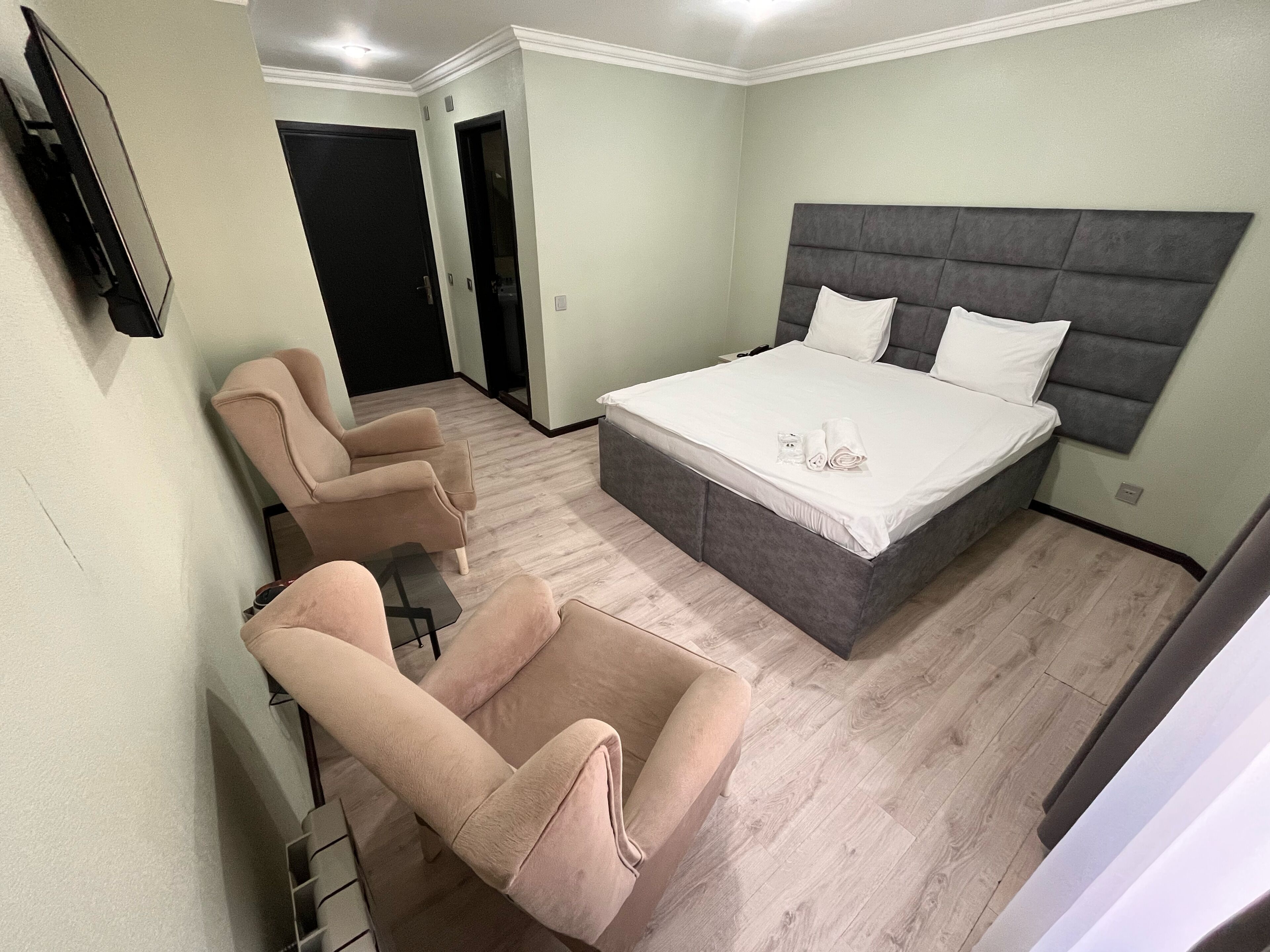 A bedroom with a bed, two armchairs, a television, and a door.