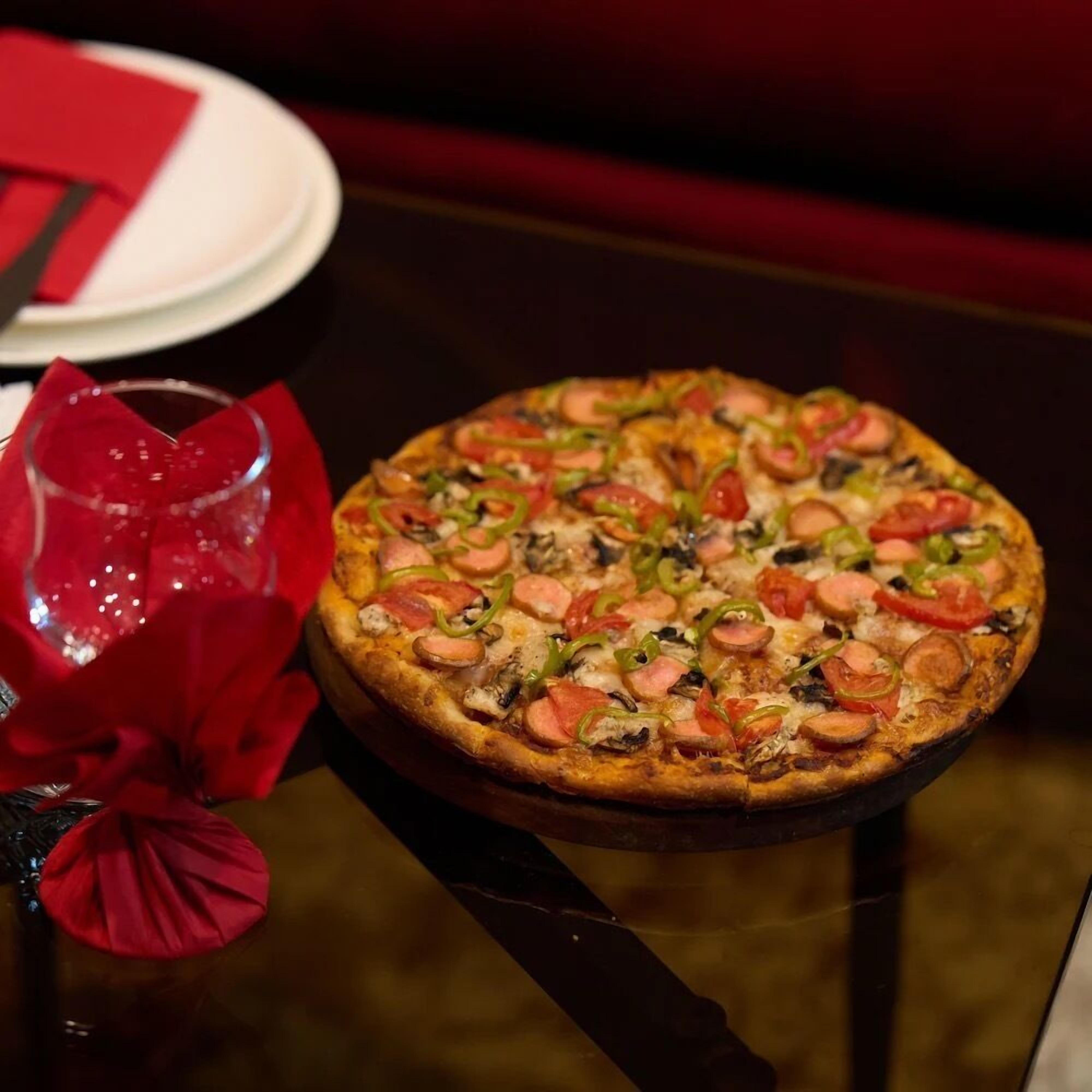 A pizza on a black table with a red napkin and a glass.
