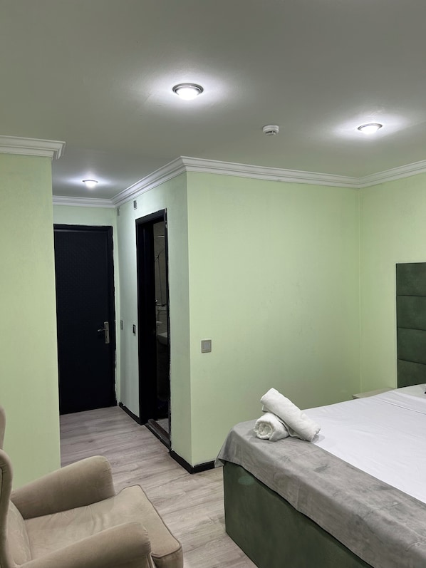 A hotel room with a bed, a chair, a door, and a light fixture on the ceiling. - Rosemary Inn (Baku)