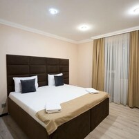 Habitación de hotel con una cama grande, cabecera, mesita de noche y ventana con cortinas.