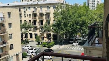Ein Balkon mit Blick auf ein mehrgeschossiges Gebäude, eine Straße mit Autos und etwas Grün.