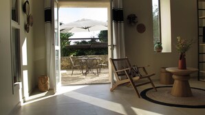 Ein Zimmer mit einer Schiebetür zu einer Terrasse, ein Korbstuhl, ein kleiner runder Tisch mit einer Vase und ein Bücherregal.