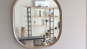 Ein runder Spiegel an einer Wand, der einen Raum mit einer Bank, einem kleinen Tisch und einem Regal mit verschiedenen Gegenständen widerspiegelt.