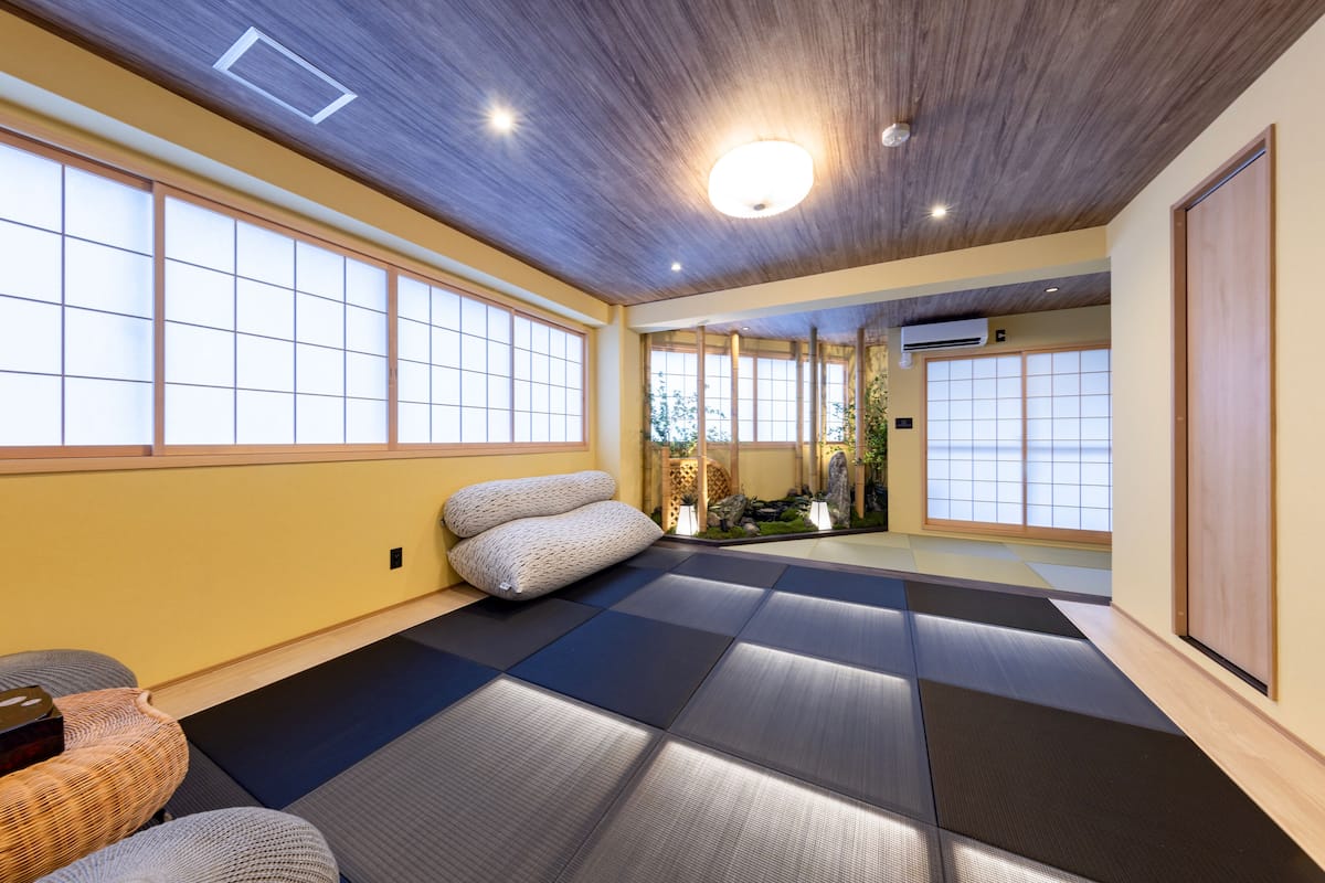 Una habitación con esteras de tatami, puertas correderas, un sofá de tatami y un pequeño jardín interior.