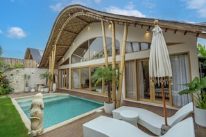Een moderne villa met een zwembad, buitenmeubels en grote ramen.