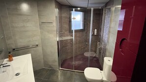 Ett modernt badrum med en dusch som är avskärmad med glasväggar, ett vitt handfat och en toalett.