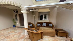 A covered patio area with wicker furniture, a potted plant, and a window with barred glass. - Villa Bolet        . (Chiclana de la Frontera)