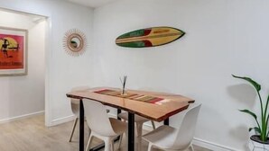 Een eethoek met een houten tafel, witte stoelen en een surfboarddecoratie aan de muur.