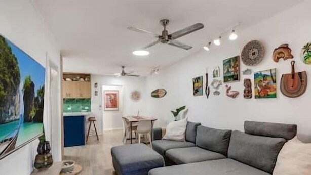Een moderne woonkamer met een grijze modulaire bank, een eethoek met een tafel en stoelen, en een keuken op de achtergrond.