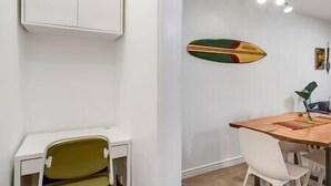 Een eetruimte met een houten tafel, witte stoelen en een surfboard decoratie aan de muur.