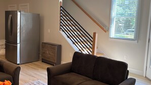 A modern living room with a dark brown sofa, a wooden coffee table, and a patterned rug. A stainless steel refrigerator is visible in the background. - Downtown Escape - 5 blocks to Riverwalk (Wilmington)