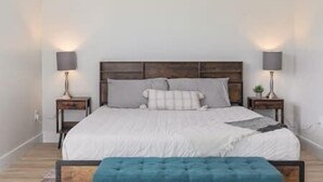 A bedroom with a large bed, two bedside tables with lamps, and a blue bench in front of the bed. - Downtown Escape - 5 blocks to Riverwalk (Wilmington)