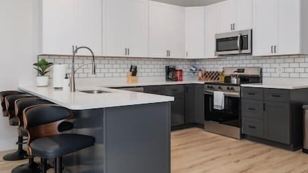 A modern kitchen with white cabinets, a central island with bar stools, a microwave, and a stove. - Downtown Escape - 5 blocks to Riverwalk (Wilmington)