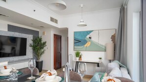 A modern hotel room with a dining area, a flat-screen TV, a large abstract painting, and a cozy seating area with a sofa and a chair.