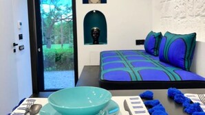 Een kleine kamer met een bed, een raam, een kom en een lepel op een tafel.