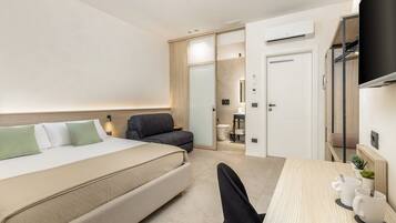 Una habitación de hotel con cama, escritorio, silla, pequeño sofá, equipo de aire acondicionado y armario.