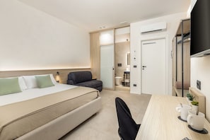 Una habitación de hotel con cama, escritorio, silla, pequeño sofá, equipo de aire acondicionado y armario.