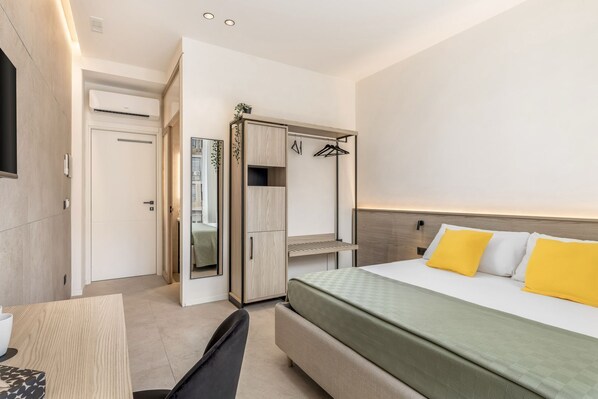 Una habitación de hotel con cama, escritorio, silla, armario y espejo.