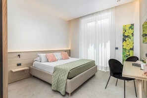 Una habitación de hotel con cama, mesita de noche, silla y escritorio con asiento.