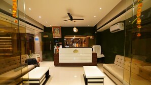 A hotel reception area with a reception desk, sofas, and a ceiling fan. - Hotel Grand Maratha  (Nanded)