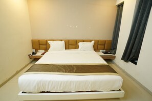 A hotel room with a large bed, a wooden headboard, a bedside table with a phone, and a window with curtains. - Hotel Grand Maratha  (Nanded)