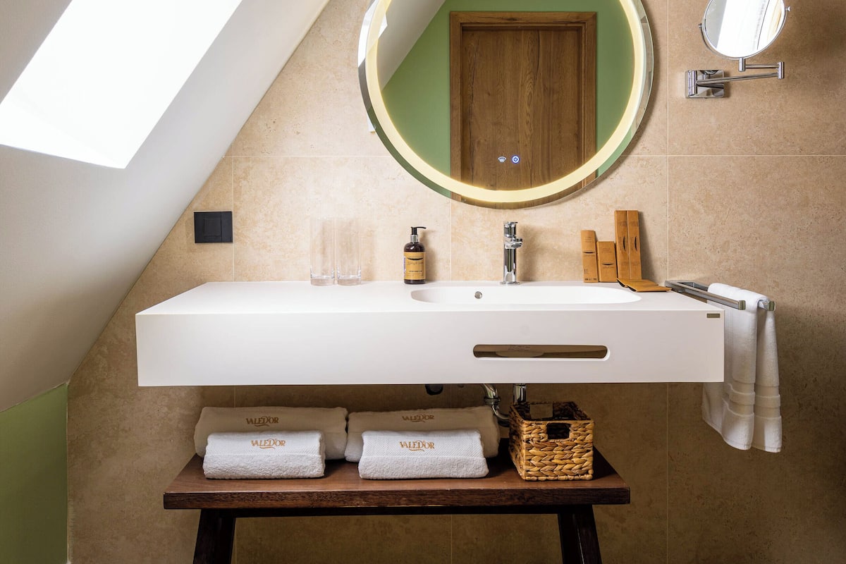 A modern bathroom with a skylight, a round mirror, a white sink, and a wooden vanity.