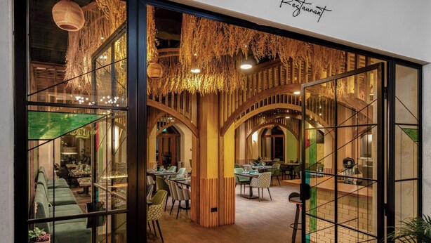 Un ristorante dall'arredamento moderno, con archi in legno, sedute verdi e decorazioni pensili.