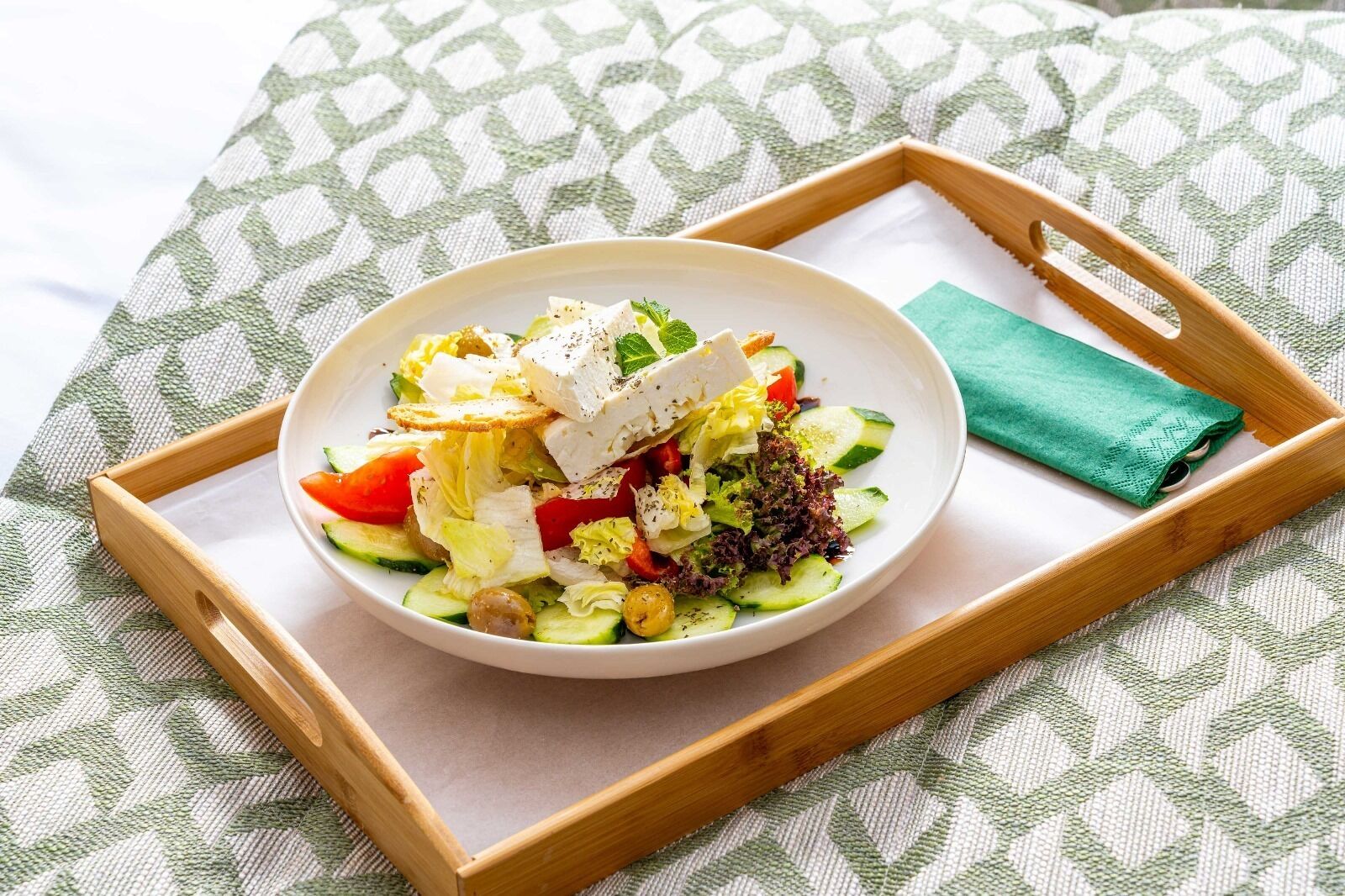 Ensalada con queso feta, pepinos, tomates y aceitunas sobre una bandeja de madera.