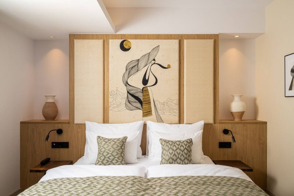 A modern hotel room with a large bed, two nightstands, a wooden headboard with artwork, and bedside tables with vases.