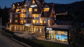 Un hotel a più piani con una facciata ben illuminata, balconi e una zona piscina visibile.