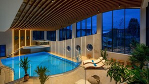 Una piscina interna moderna con soffitto in legno, ampie finestre e vista sul paesaggio esterno.