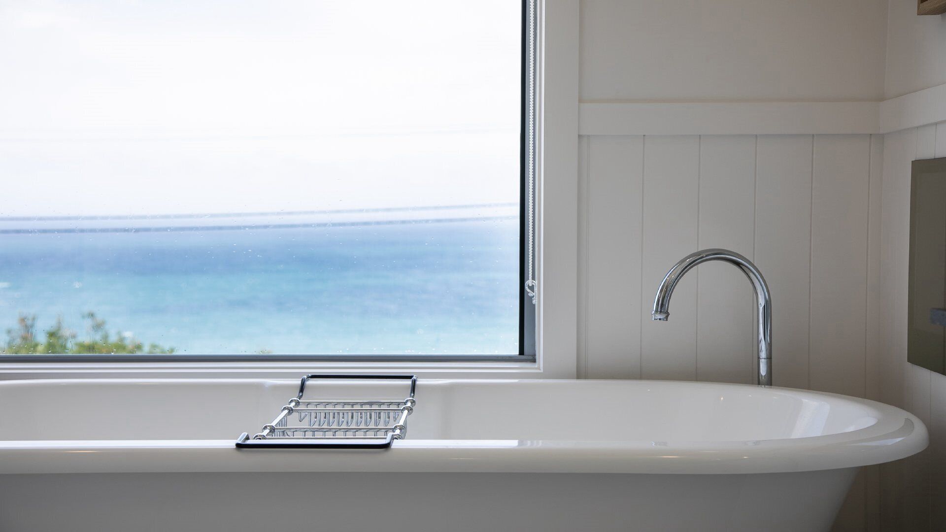 Une salle de bain avec une baignoire sur pieds, une fenêtre donnant sur la mer et un porte-serviettes.