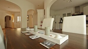 Une pièce spacieuse avec une table à manger en bois, des chaises blanches et un coin cuisine à l’arrière-plan.